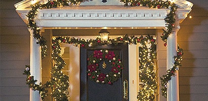 Exterior entry way of a home with garland and white Christmas lights hung using Command™ light clips.