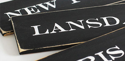 Three black painted pine boards with the transferred city names painted in white.